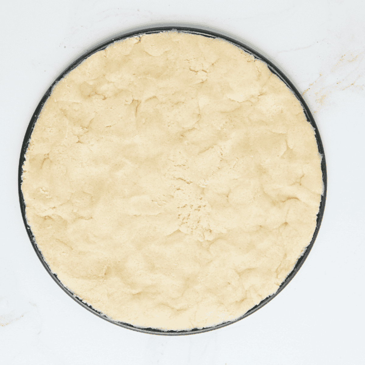 Small pizza pan sprayed with cooking spray, half covered with cookie dough.