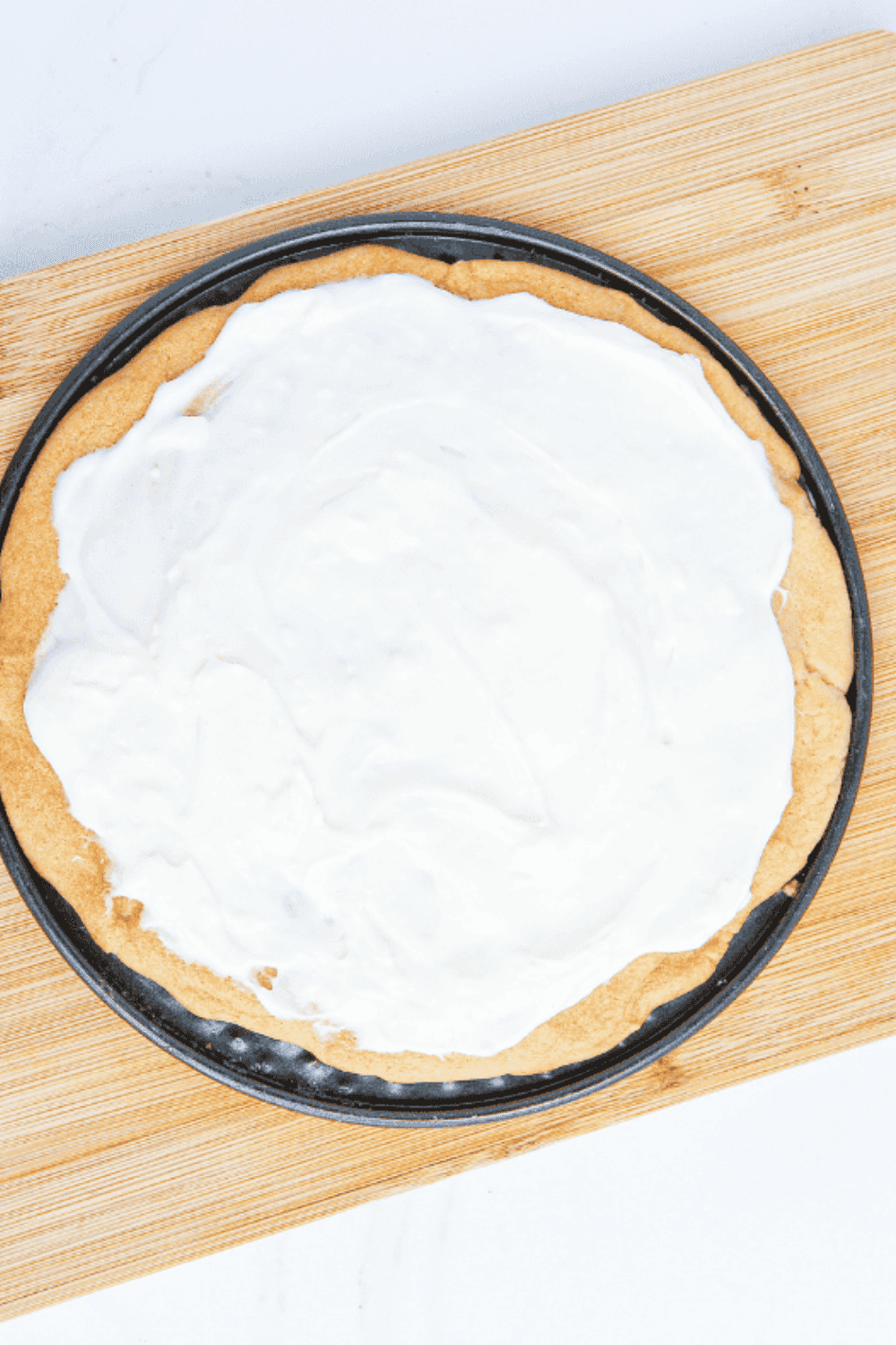 Cooled cookie crusts being topped with a smooth, creamy mixture of cream cheese, sugar, and vanilla.