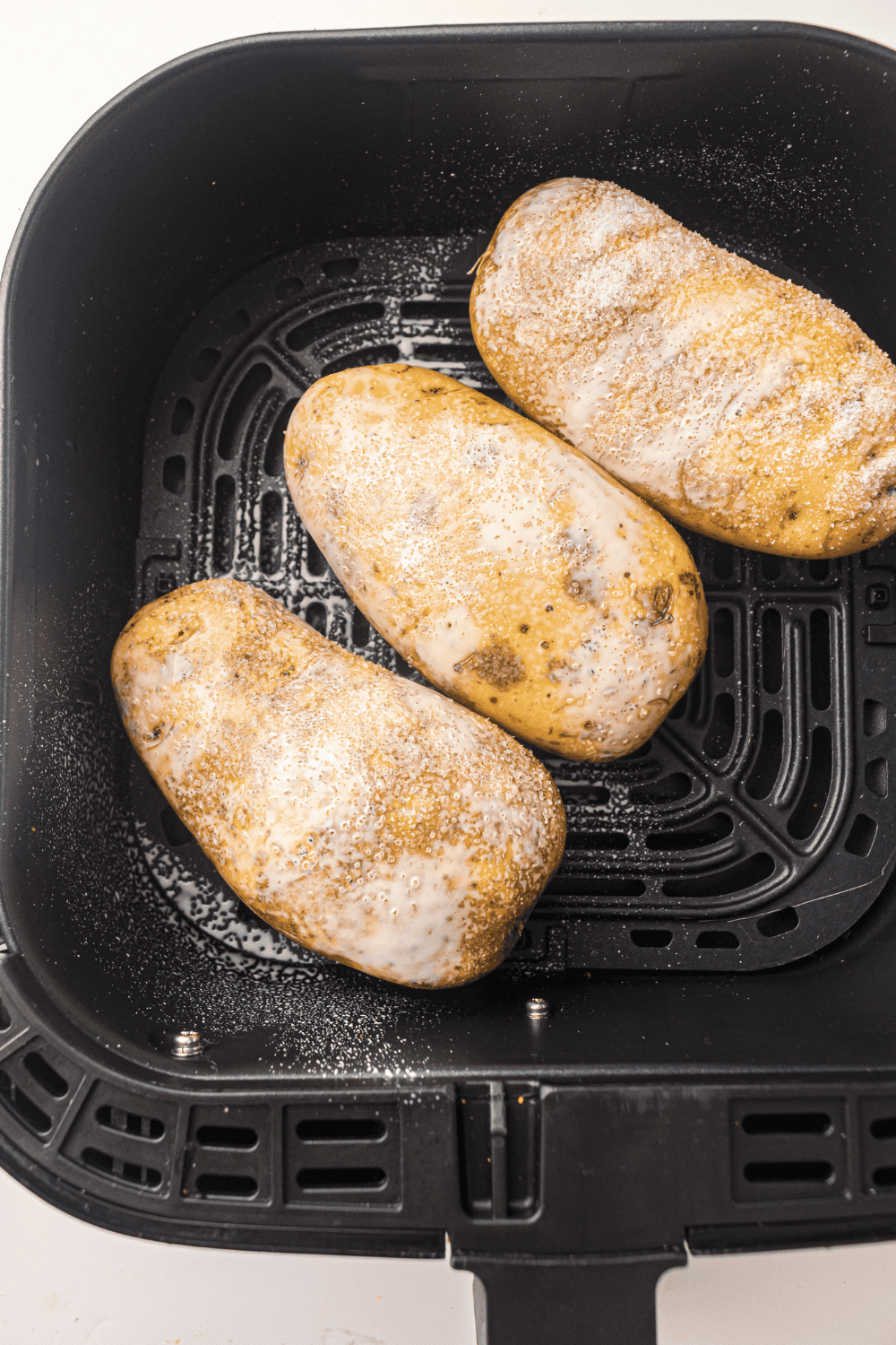 Potatoes being brushed with olive oil and sprinkled with salt before air frying.