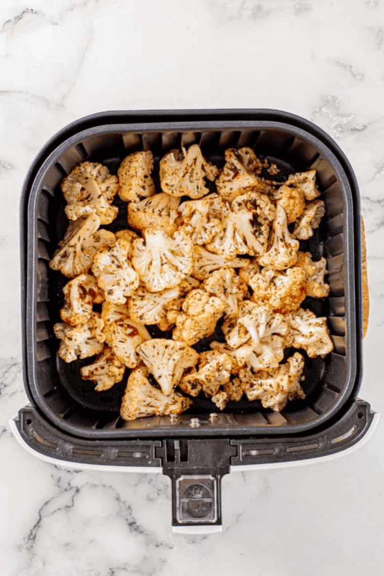 Cauliflower and tomatoes cooking in the air fryer, lightly charred and crisp after shaking the basket.