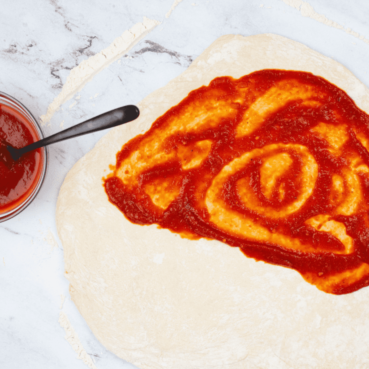 Pizza dough rolled into a 10–12 inch circle on a floured surface, ready for filling.
