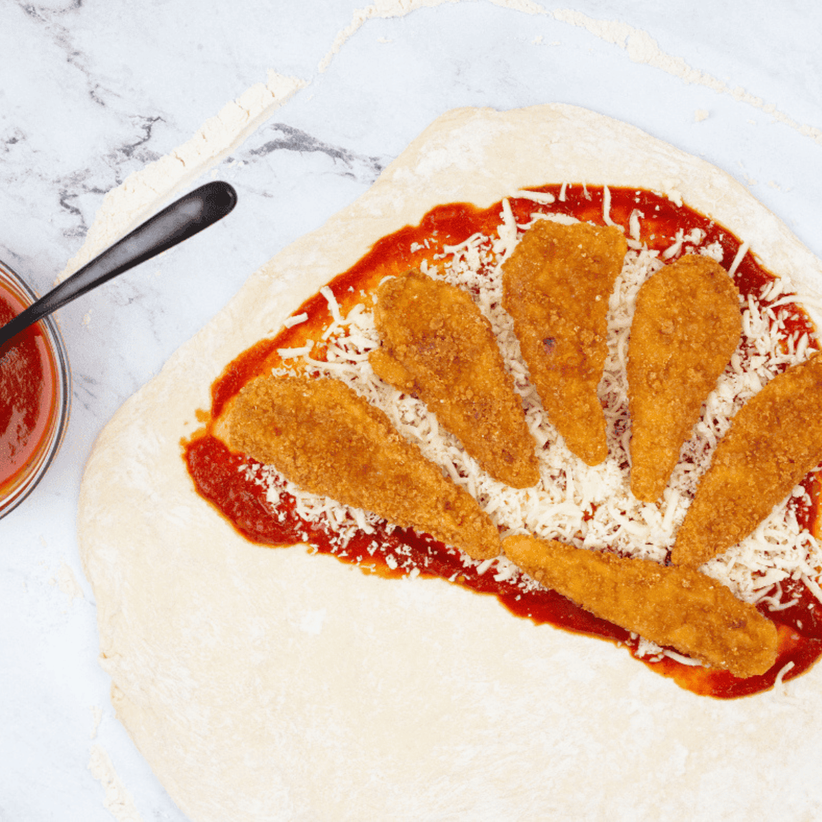 Pizza dough half topped with sauce, cheese, and chicken tenders, folded over and sealed to form a calzone.
