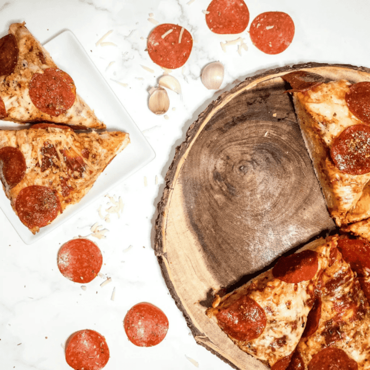 Spatula lifting a finished air fryer pan pizza out of the pan, showing the crispy browned bottom crust