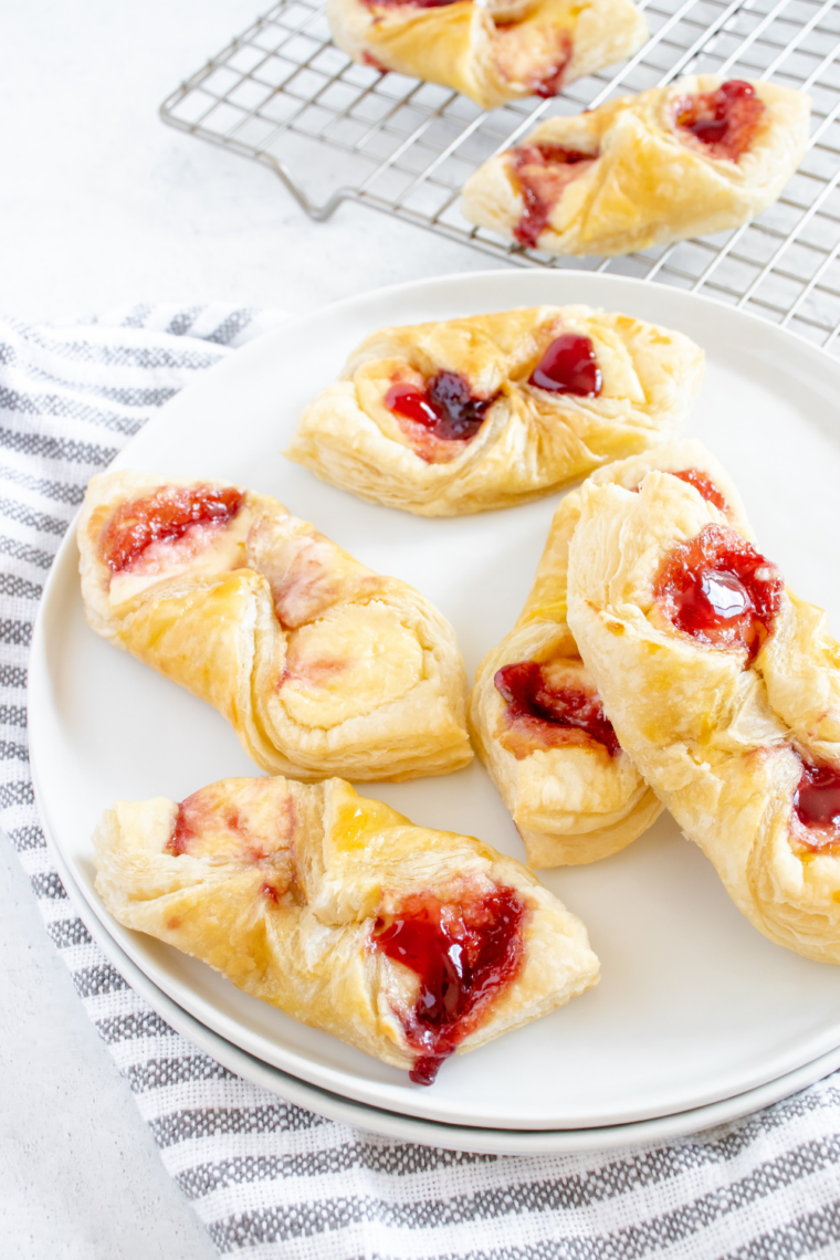 Four flaky puff pastry Danish on a white plate with vanilla glaze drizzled on top