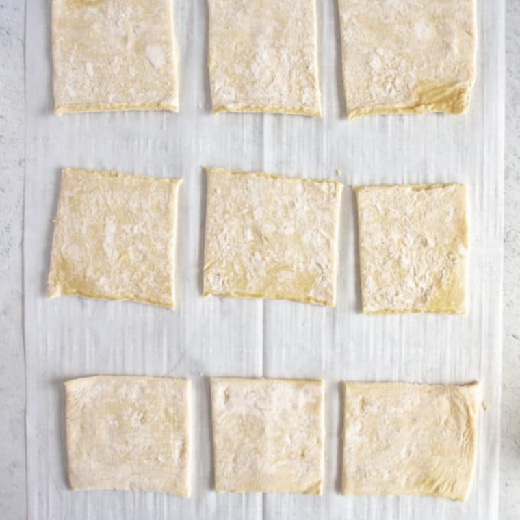 Puff pastry sheet cut into nine equal squares with a pizza cutter on a floured board