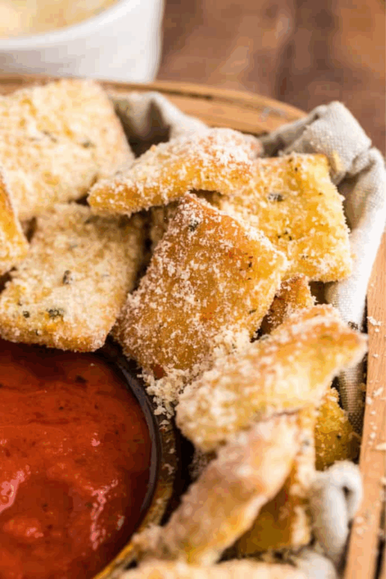 A pile of small, golden-brown homemade Domino's style garlic bread knots, heavily brushed with garlic butter and topped with Parmesan cheese and dried herbs.