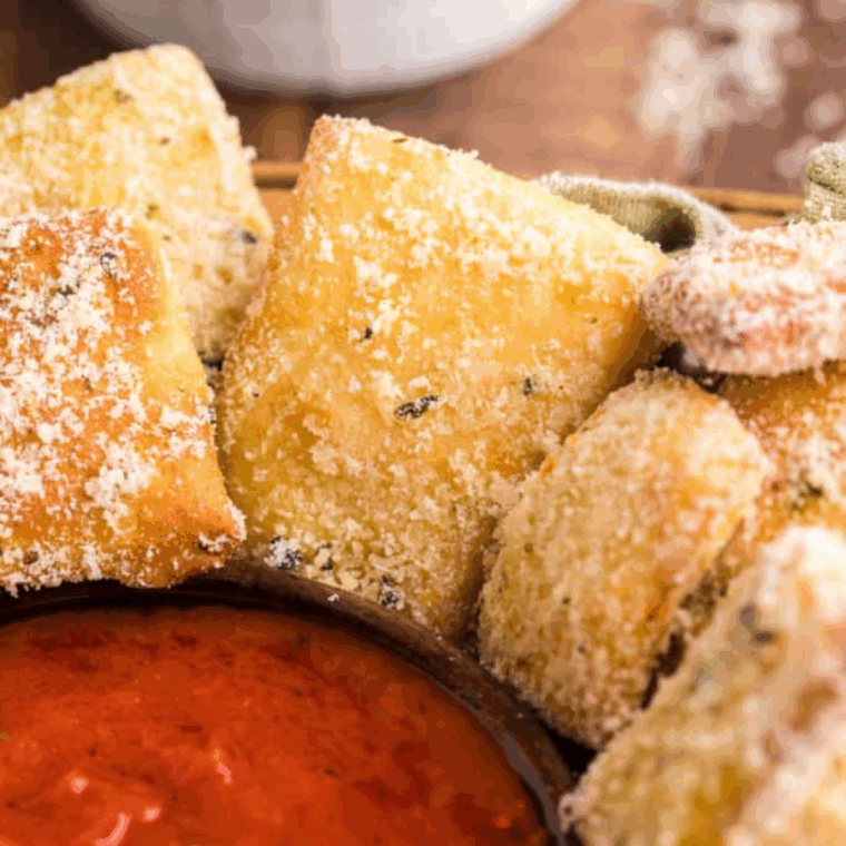 A pile of small, golden-brown Copycat Domino's Parmesan Bread Bites, brushed with garlic butter and dusted heavily with grated Parmesan cheese and herbs.