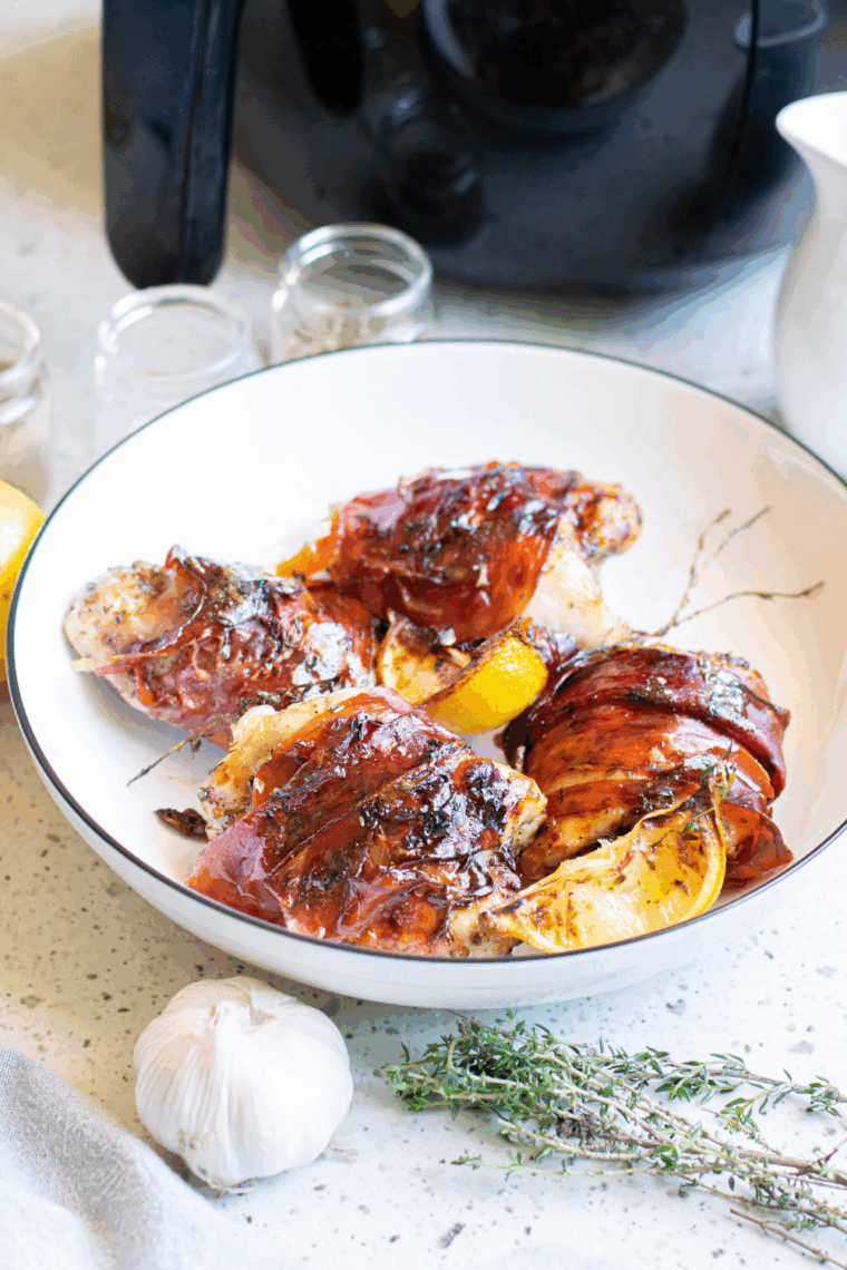 Bacon wrapped chicken thighs arranged in an air fryer basket