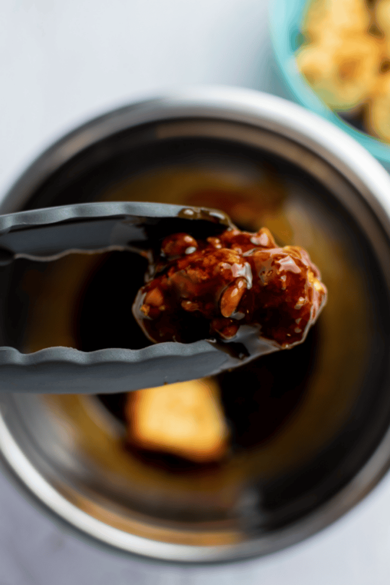 Air fryer cauliflower florets being coated in teriyaki sauce and returned to the air fryer for glazing.