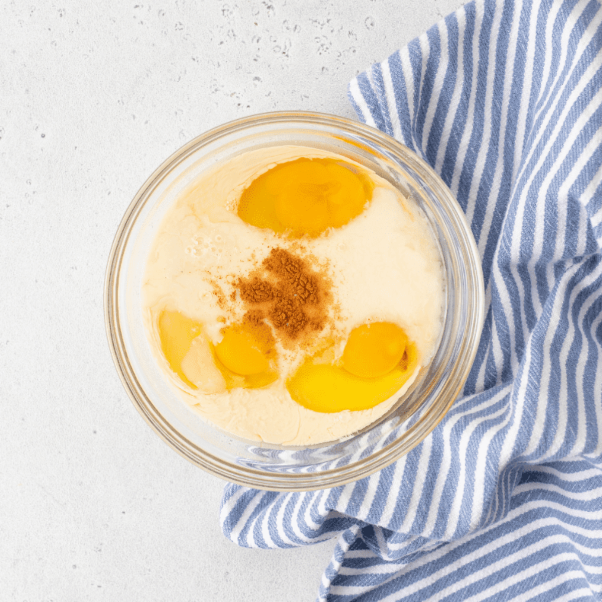 Baking dish sprayed with cooking spray and custard mixture of eggs, milk, vanilla, and cinnamon being prepared in a large bowl