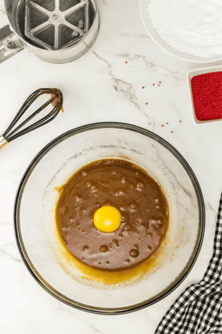 Mixing bowl with sugar, butter, molasses, and egg yolk, with dry ingredients being sifted into the mixture.