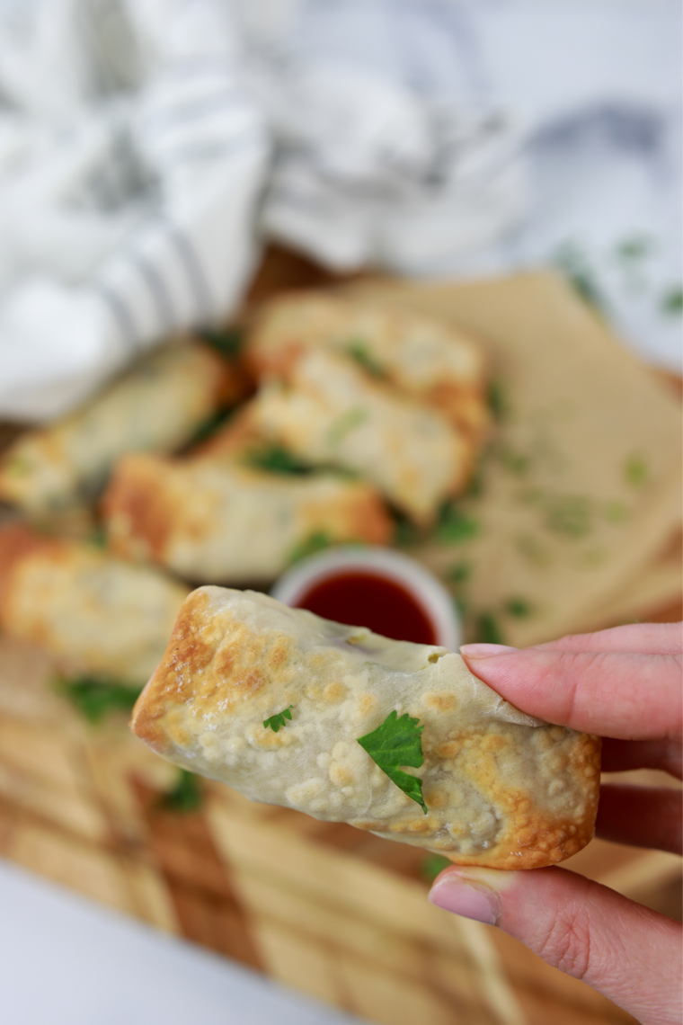 Hand holding a crispy air fryer chicken cilantro egg roll dipped in cilantro lime sauce