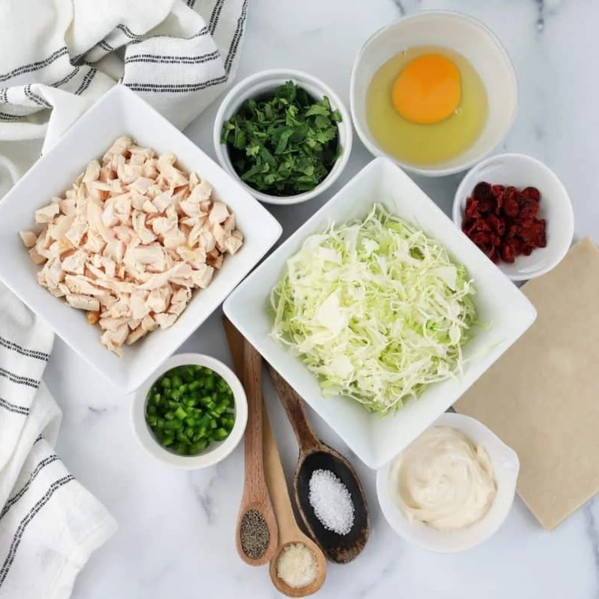 Shredded chicken, cilantro, cabbage, jalapeño, and dried cranberries laid out for egg roll filling