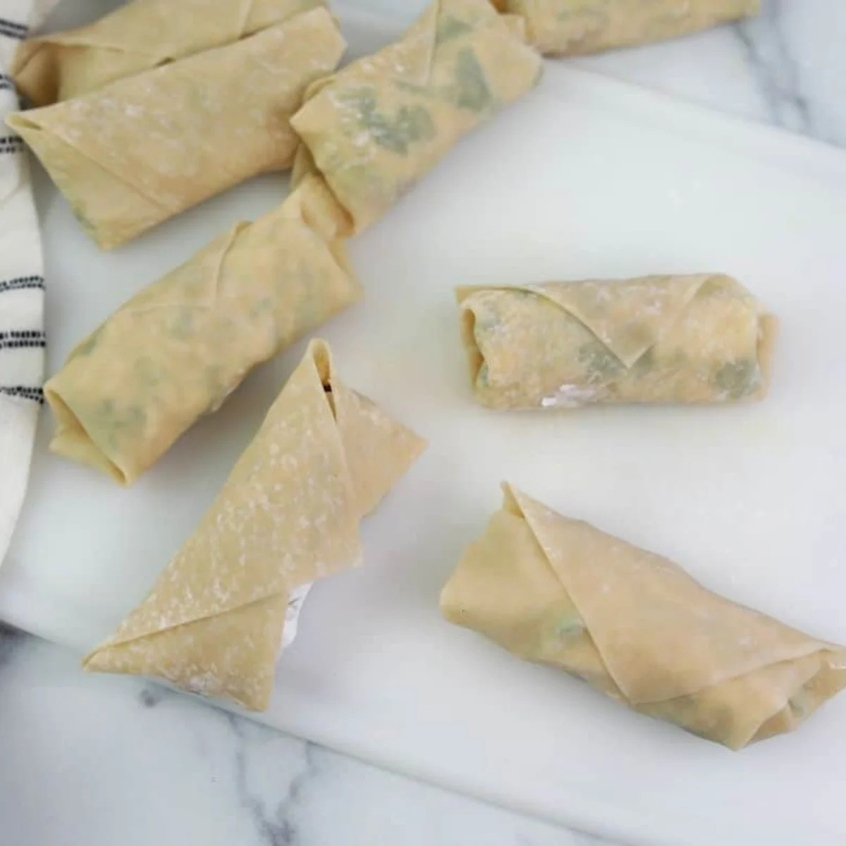 Hands folding the sides of an egg roll wrapper inward before rolling it closed