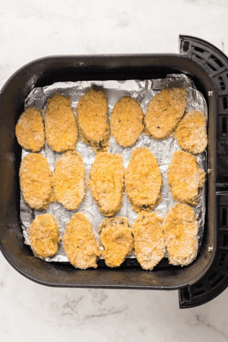 Breaded pickles in a single layer in the air fryer basket, sprayed with oil at 400°F