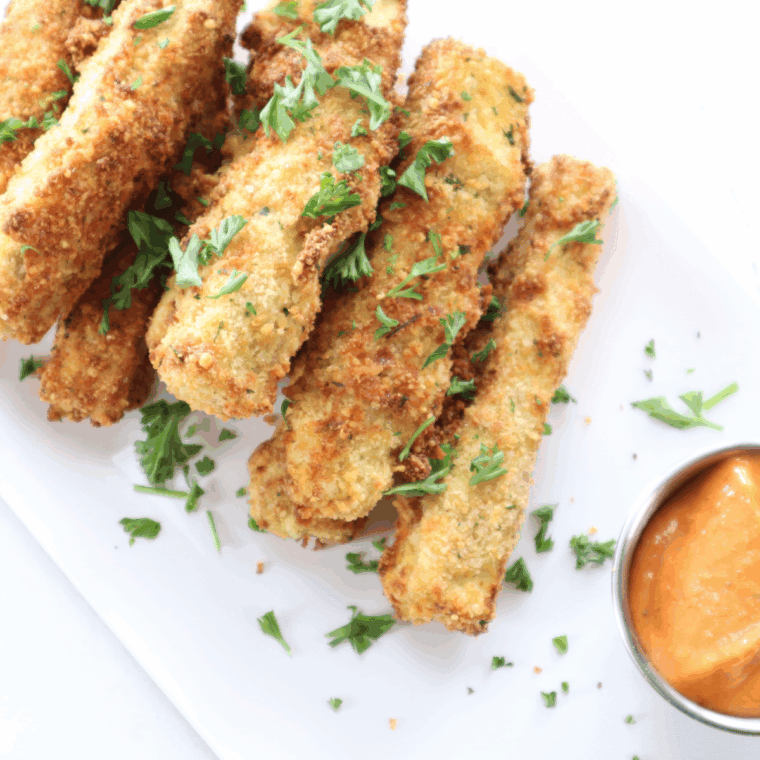 Golden and crispy air fryer eggplant fries served on a plate with dipping sauce.