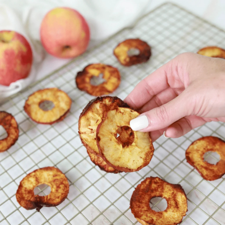 Thin apple slices sprinkled with cinnamon in an air fryer basket, turning into crispy apple chips.