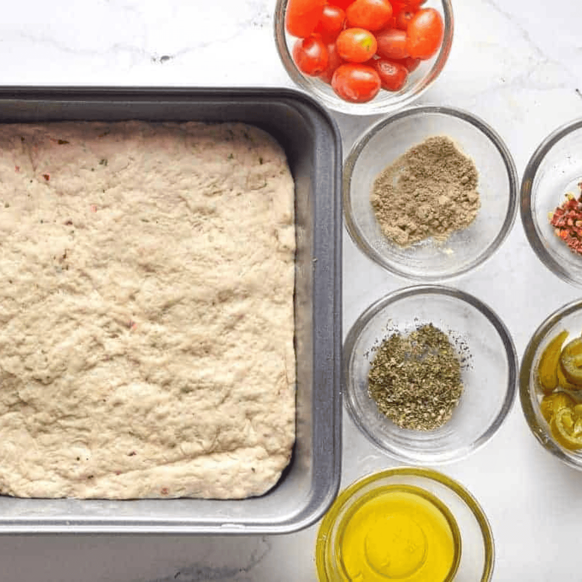 Placing focaccia dough into an oiled pan, spreading it evenly, and making finger indentations on top.
