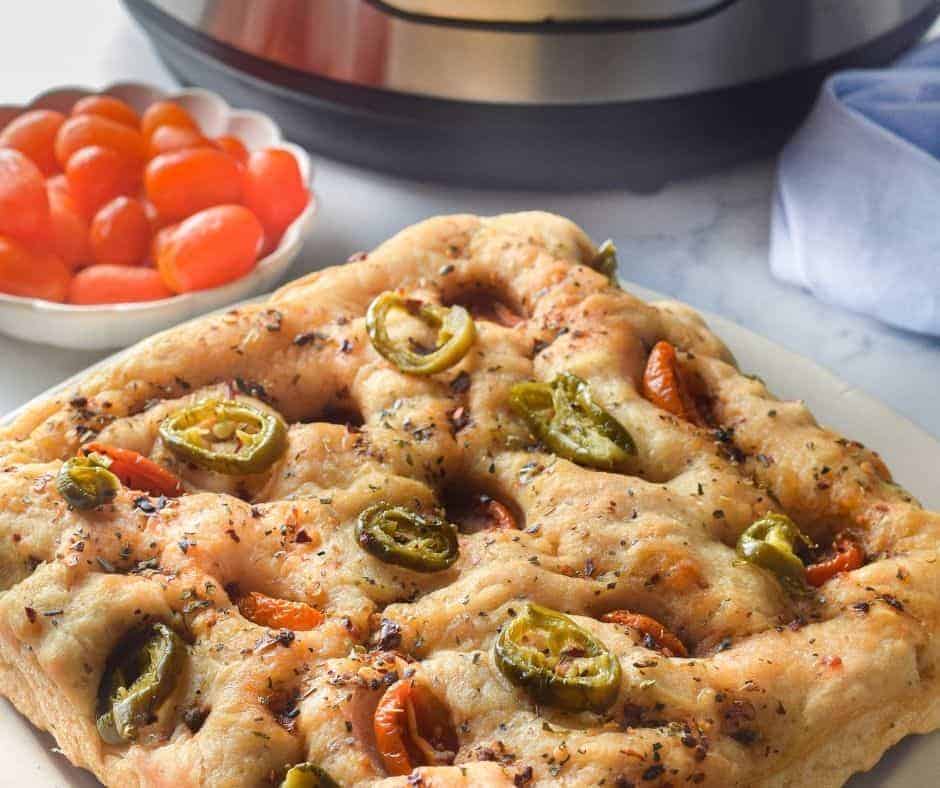 Freshly baked golden focaccia bread made in the Instant Pot, topped with herbs and vegetables, ready to serve.