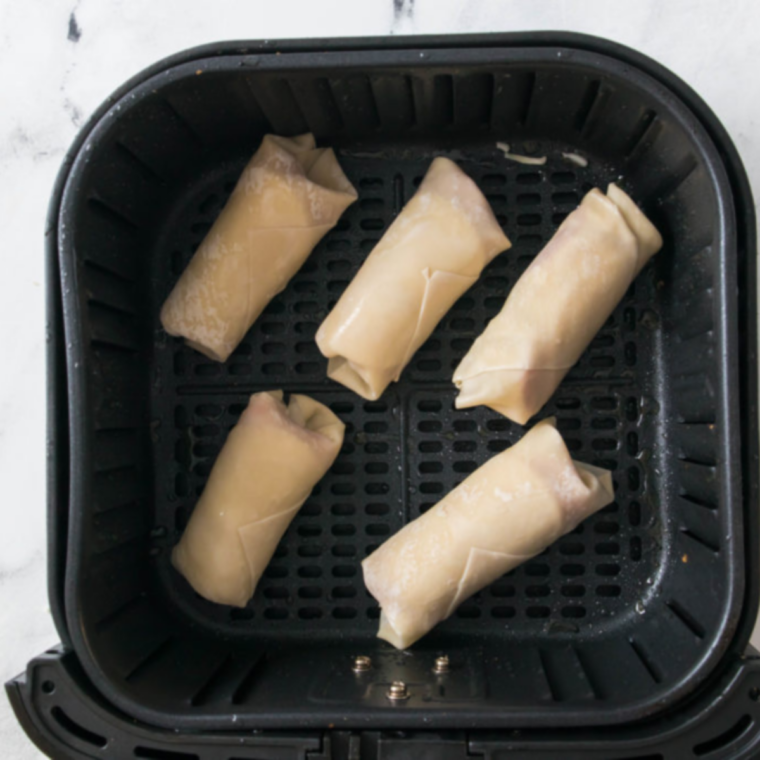 Antipasto egg rolls arranged seam side down in an air fryer basket before cooking at 400°F