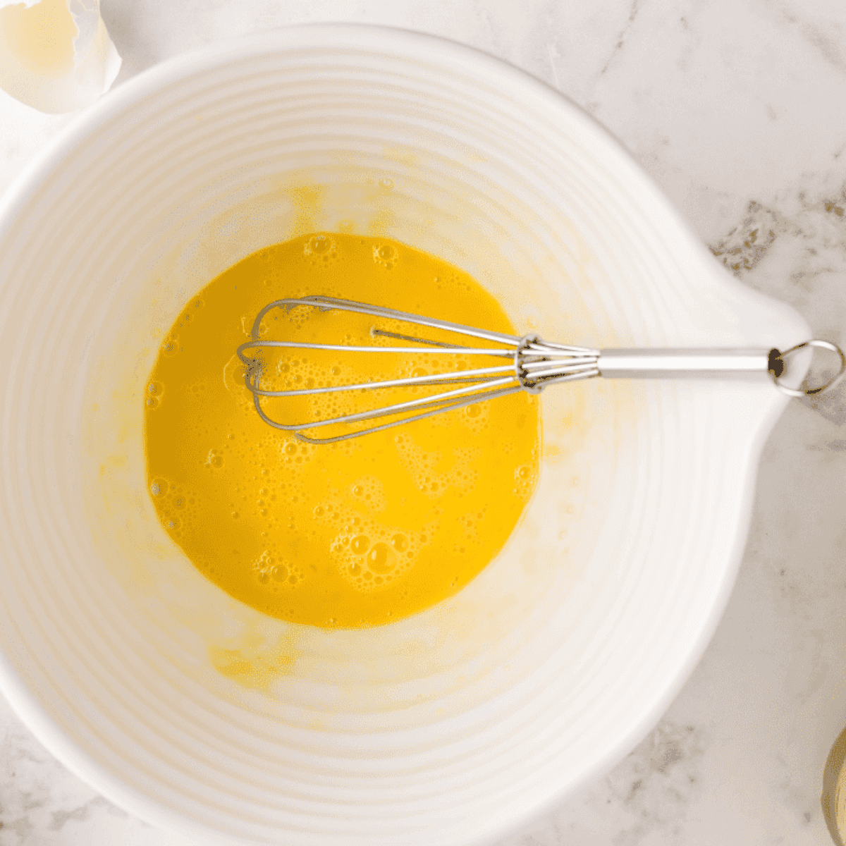 Whisking eggs and melted butter together in a large mixing bowl