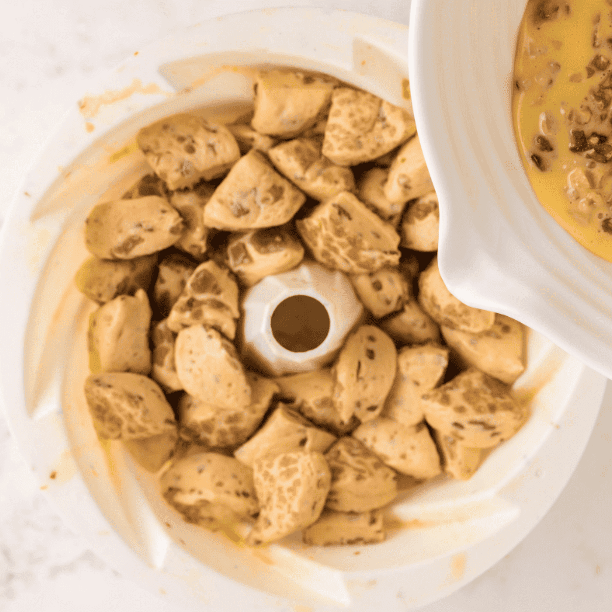 Cinnamon roll pieces coated in eggnog mixture in a Bundt pan, cooking in the air fryer