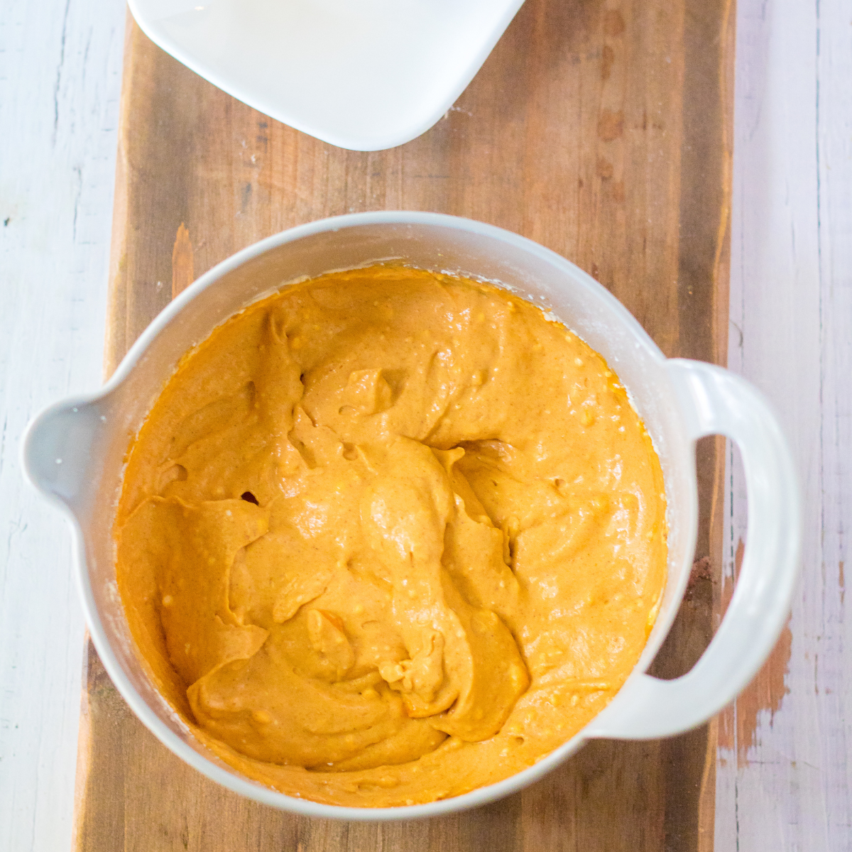 Creamy pumpkin cheesecake filling being whipped in a glass mixing bowl