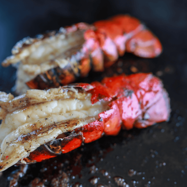 Blackstone Griddle lobster tails cooking on a flat top grill with melted garlic butter and fresh lemon wedges.