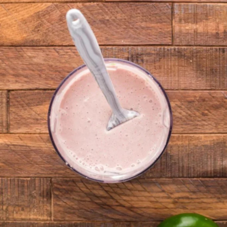 Smooth pink cranberry dip in a food processor with flecks of green jalapeno