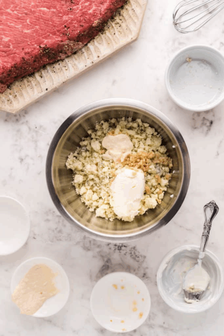 Whisking a homemade sauce mixture of blue cheese, horseradish, sour cream, and minced garlic in a bowl.