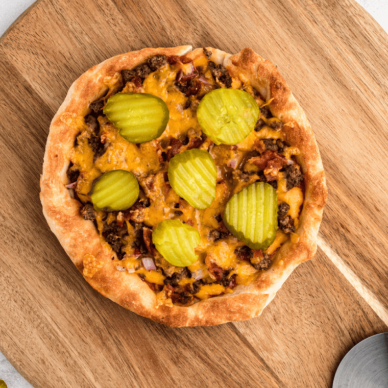 Sliced air fryer cheeseburger pizza topped with ground beef, bacon, cheddar, and dill pickles
