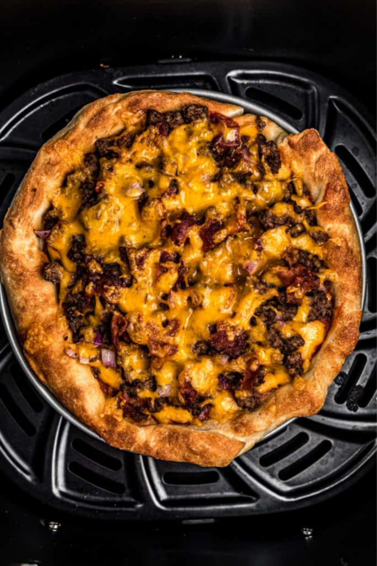 Cheeseburger pizza cooking in an air fryer basket with bubbling cheddar cheese