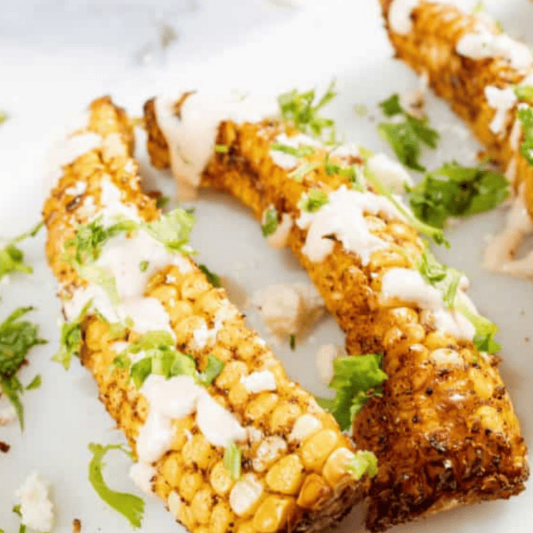 Air fryer corn ribs on a white plate topped with chipotle mayo, cotija cheese, and cilantro