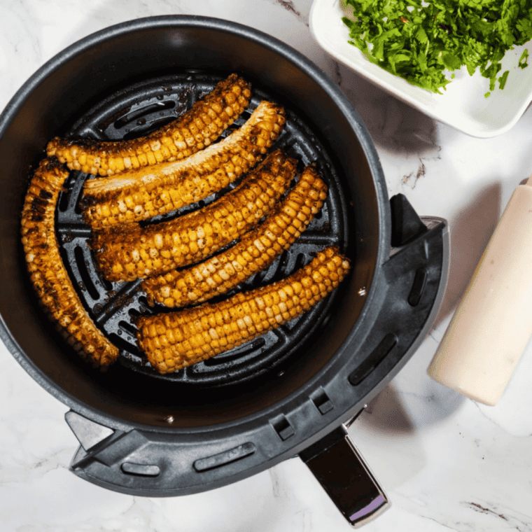 Air fryer corn ribs on a white plate topped with chipotle mayo, cotija cheese, and cilantro