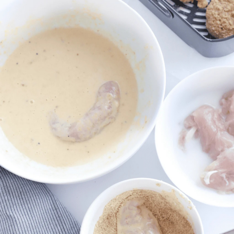 Chicken tenders soaking in seasoned buttermilk marinade in a glass bowl
