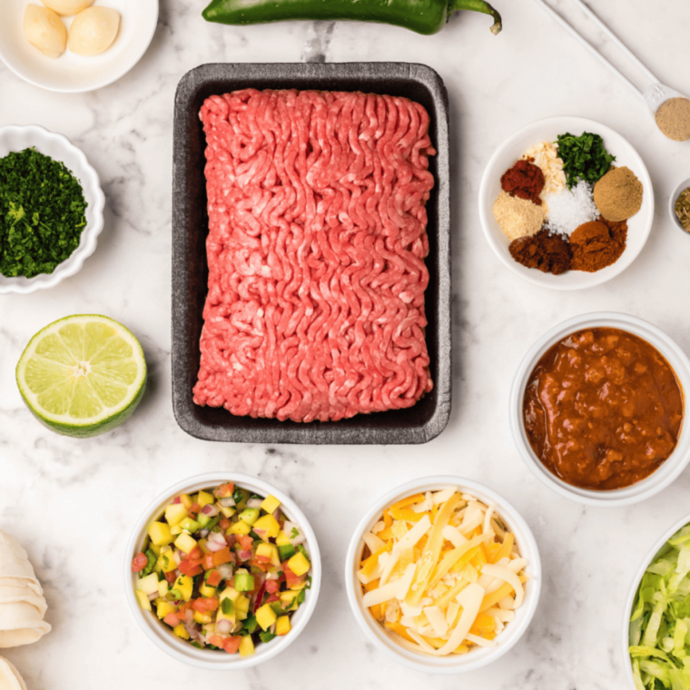 Ingredients for air fryer ground beef taco bowls, including ground beef, taco seasoning, mini shells, cheese, and toppings