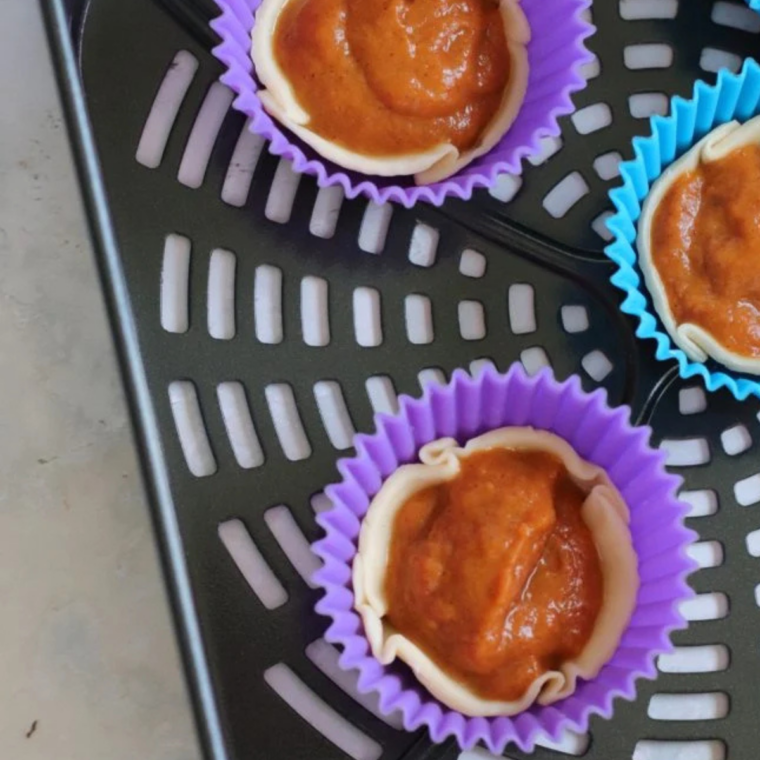 Unbaked mini pumpkin tarts arranged in an air fryer basket
