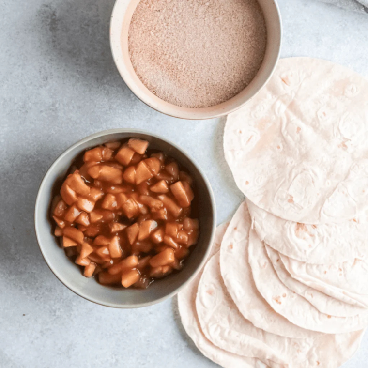 Ingredients for apple flautas including apples, flour tortillas, cinnamon, sugar, butter, and caramel sauce