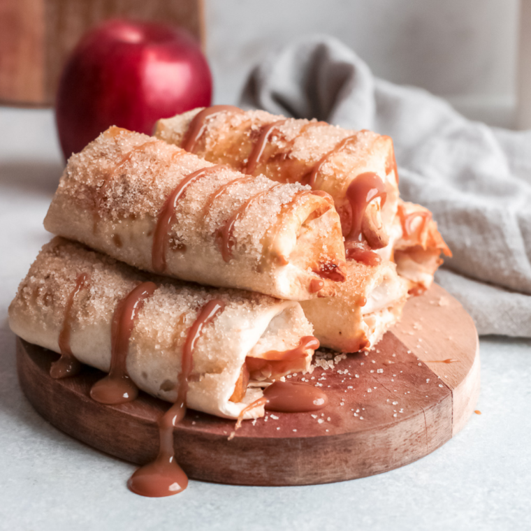 Crispy apple flautas drizzled with salted caramel sauce on a white plate
