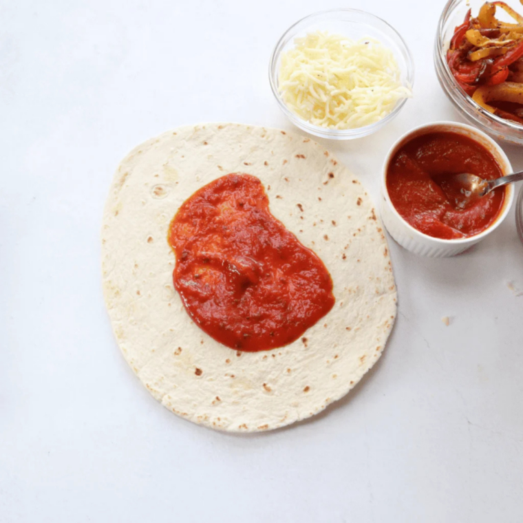 Marinara spread across the center of a flour tortilla with a clear border around the edge