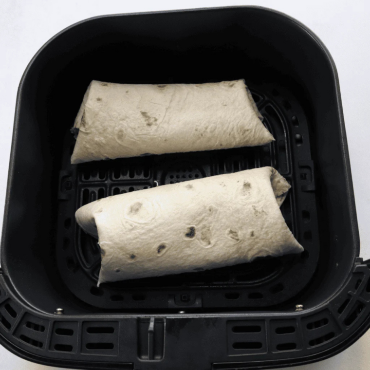 Two turkey wraps placed seam side down in an air fryer basket with space between them