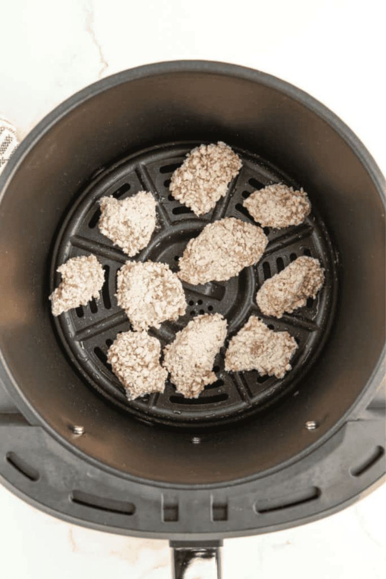 Dredged chicken pieces arranged in an oiled air fryer basket, lightly sprayed with cooking oil, ready to cook at 380°F, being shaken halfway through for even crisping.
