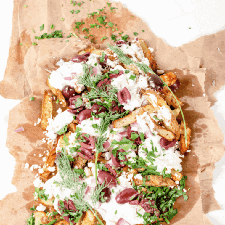 Crispy air fryer Greek fries loaded with feta, tzatziki, red onion, and parsley on a white plate