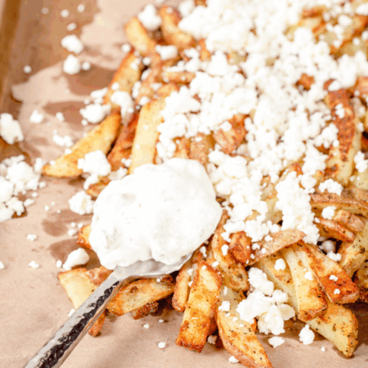 Air fryer Greek fries topped with crumbled feta, tzatziki, diced red onion, and chopped parsley