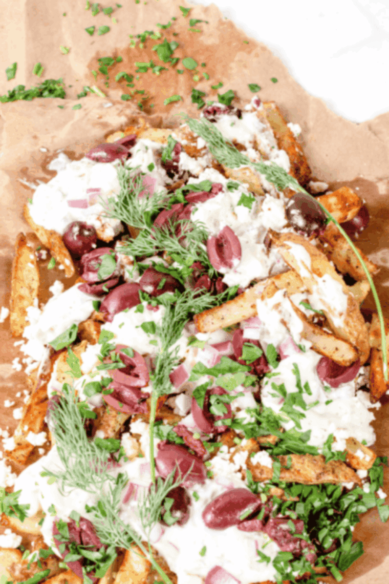 Close-up of loaded Greek fries with feta, Kalamata olives, tomatoes, and a squeeze of fresh lemon