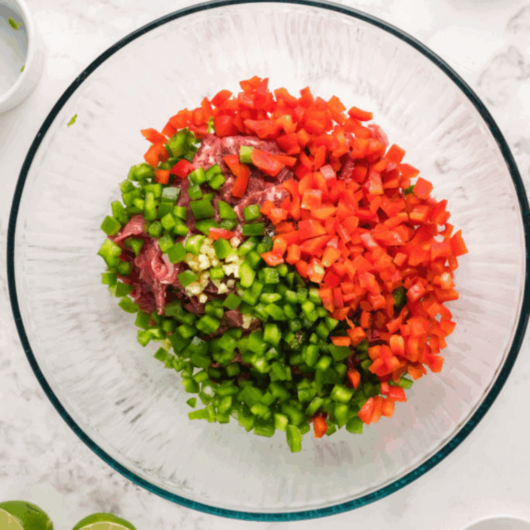 Shaved steak mixed with seasonings, garlic, onions, and peppers in a bowl, ready for the air fryer.