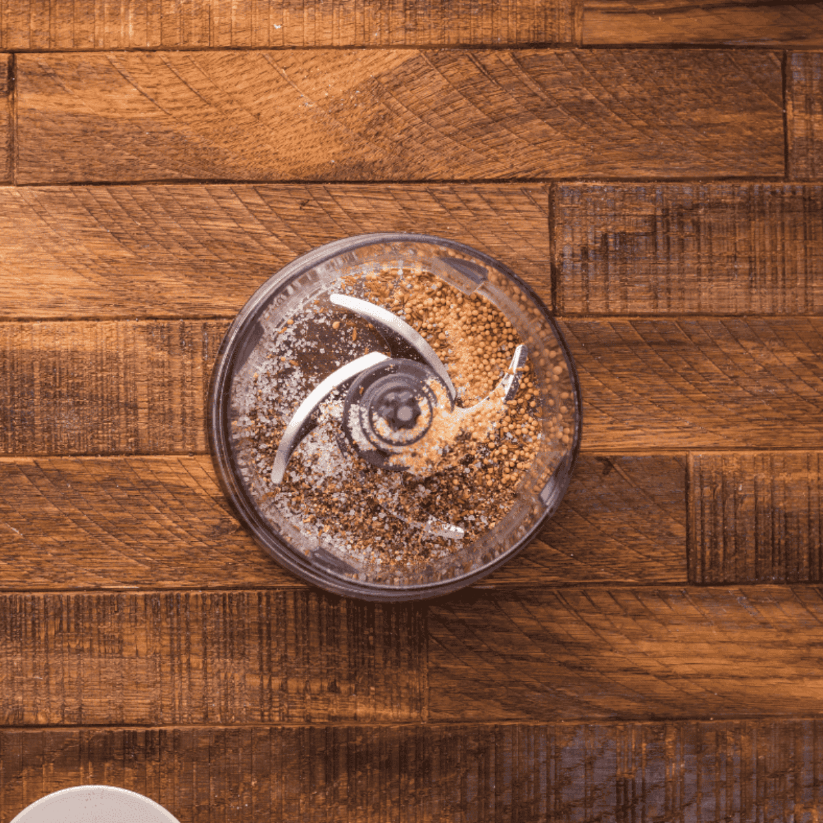 Seasoning ingredients being blended in a food processor while a frying pan heats on the stove.