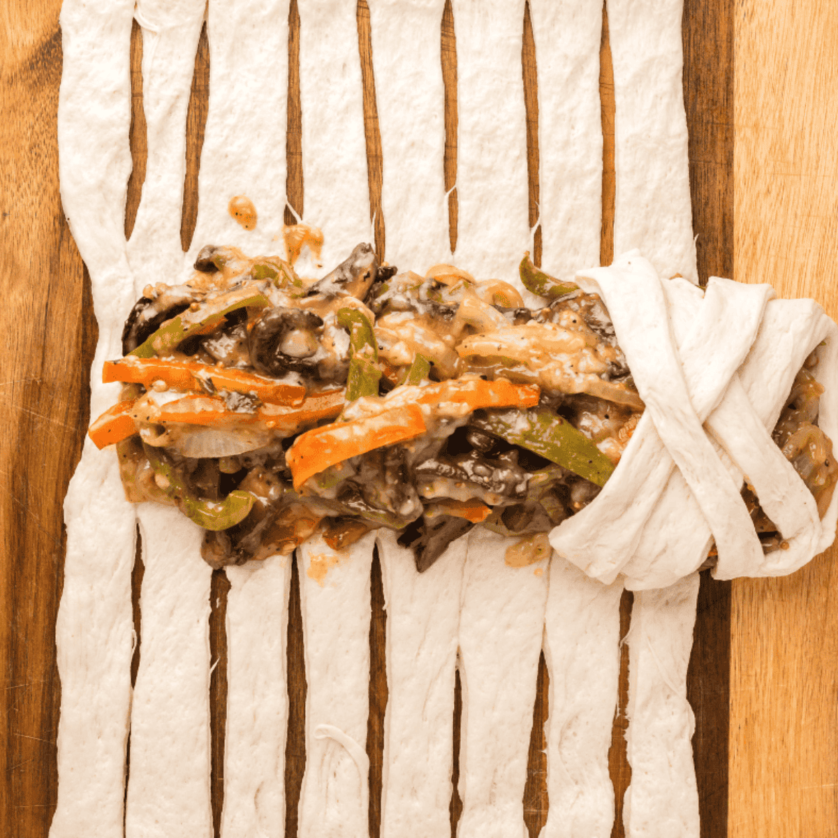 Pizza dough rolled out on a floured wooden board with strips cut along both sides.