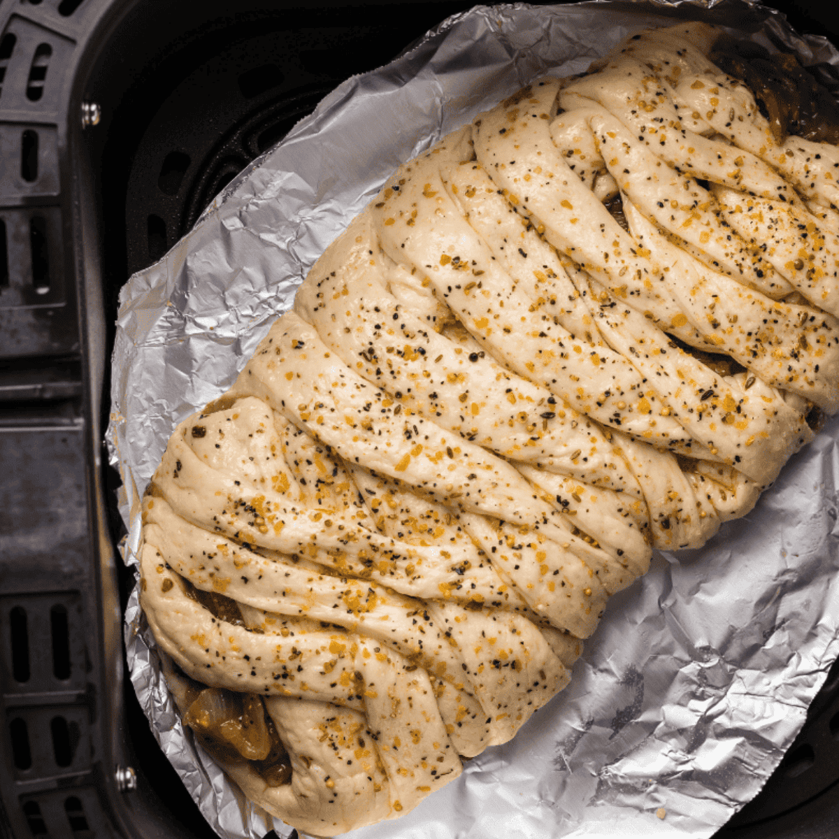 Braided pizza crust in the air fryer, brushed with olive oil, seasoned, and ready to cook, garnished with chopped parsley.