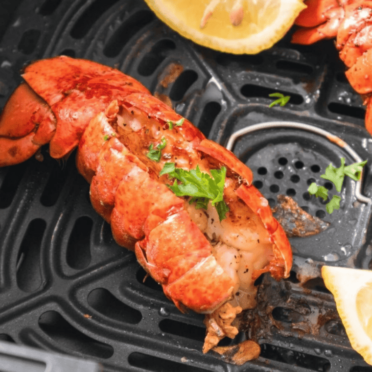 Air fryer frozen lobster tails on a white plate with melted garlic butter and lemon wedges.